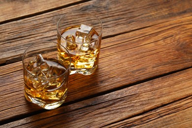 Whiskey with ice cubes in glasses on wooden table, space for text