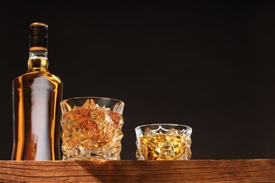 Photo of Whiskey in glasses and bottle on wooden table, low angle view. Space for text