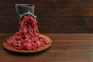 Meat grinder with beef mince on wooden table, space for text