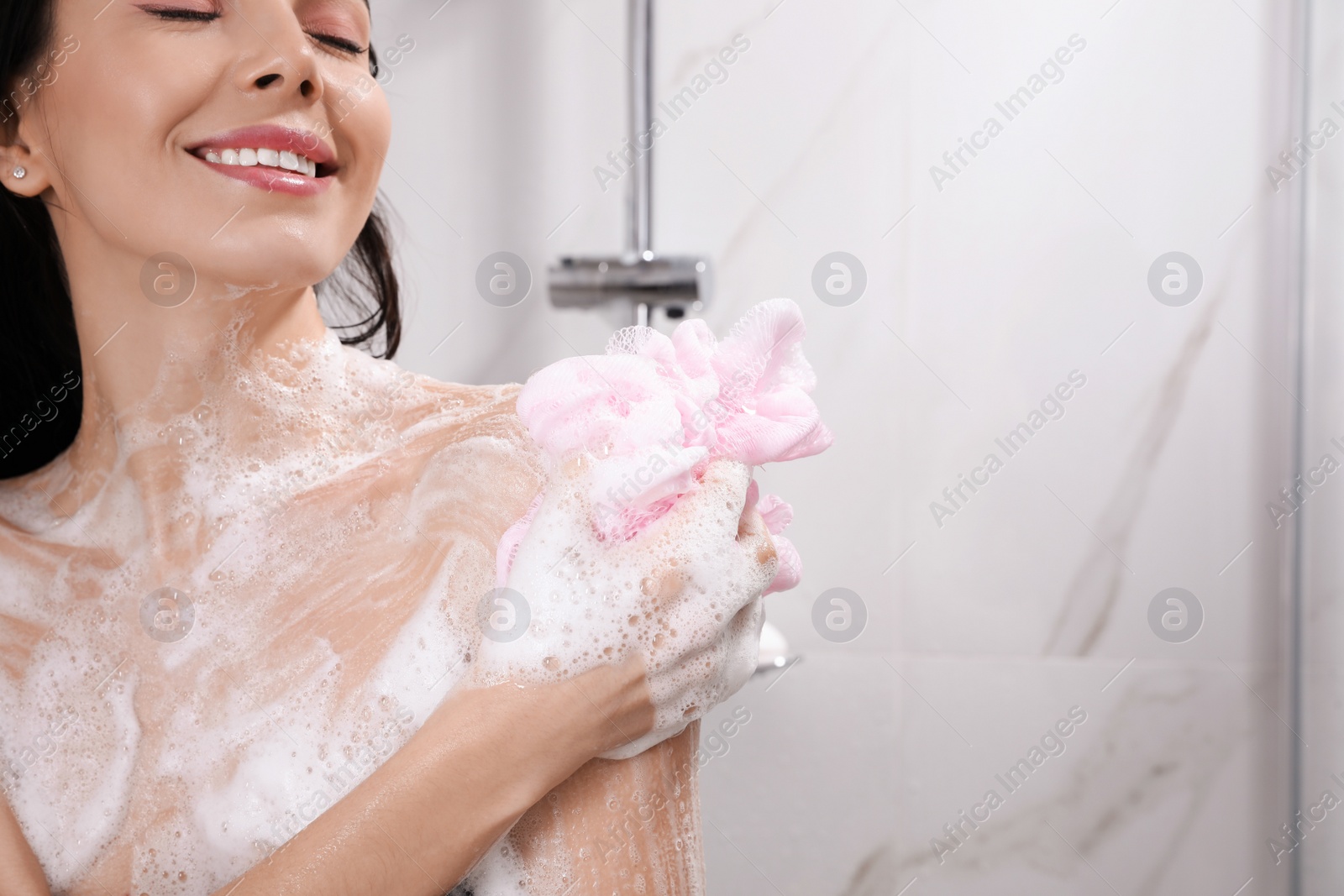 Photo of Young woman with mesh pouf taking shower at home. Space for text