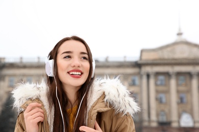 Photo of Beautiful young woman listening to music with headphones outdoors. Space for text