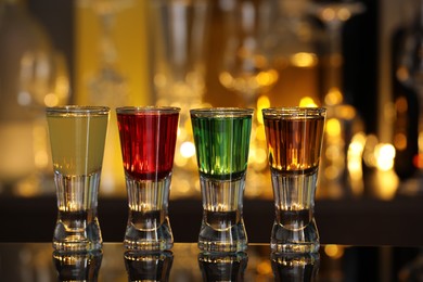 Different shooters in shot glasses on mirror surface against blurred background. Alcohol drink