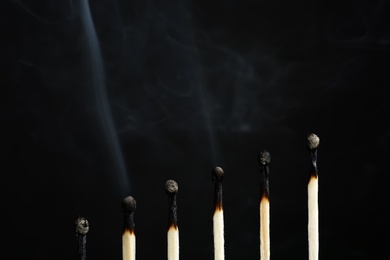 Photo of Line of burnt matches on black background. Space for text