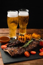 Photo of Glasses of beer, tasty fried ribs, grilled corn and sauce on wooden table