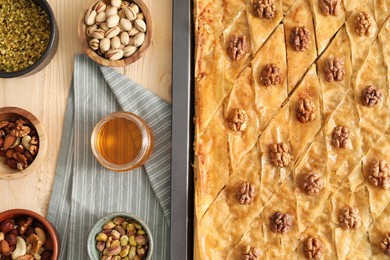 Delicious baklava with walnuts in baking pan, honey and nuts on wooden table, flat lay