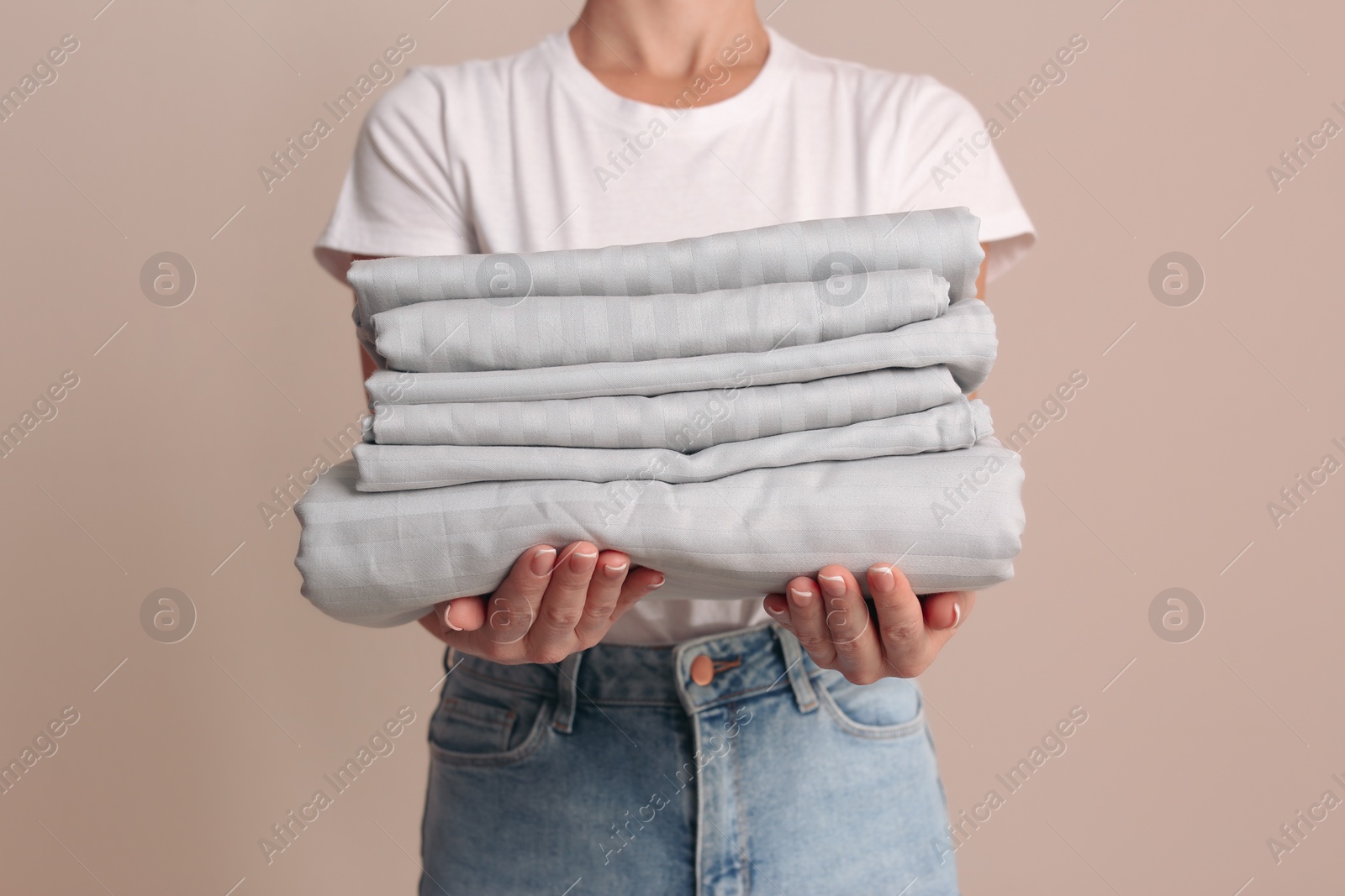 Photo of Woman holding stack of clean bed linens on beige background