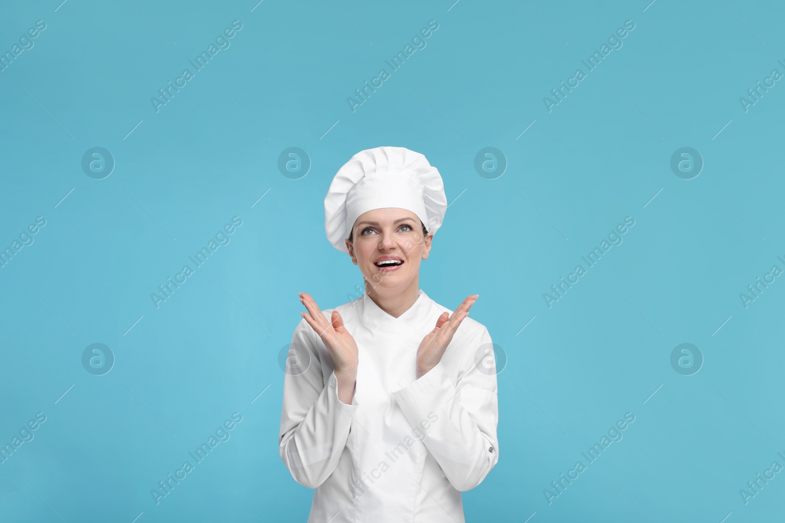 Photo of Happy chef in uniform on light blue background