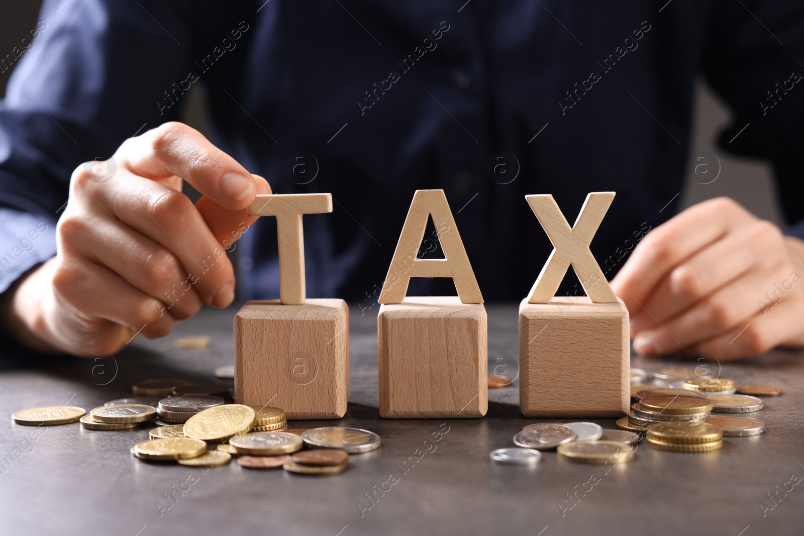 Photo of Woman with word Tax, wooden cubes and coins at grey table, closeup