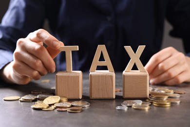 Woman with word Tax, wooden cubes and coins at grey table, closeup