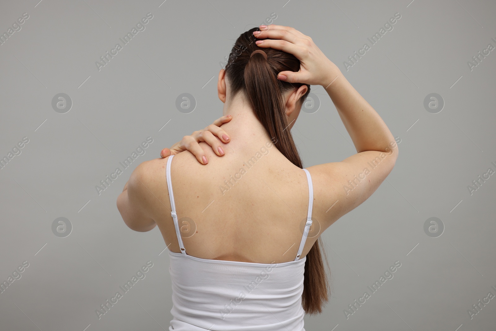 Photo of Woman touching her neck and head on grey background, back view