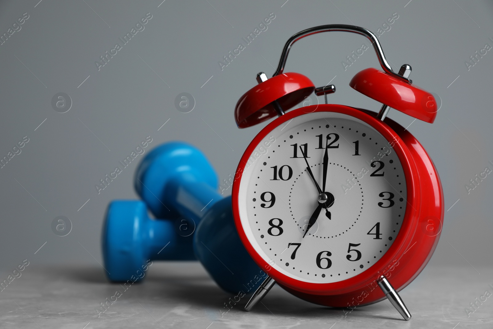 Photo of Alarm clock and dumbbells on table against grey background. Morning exercise