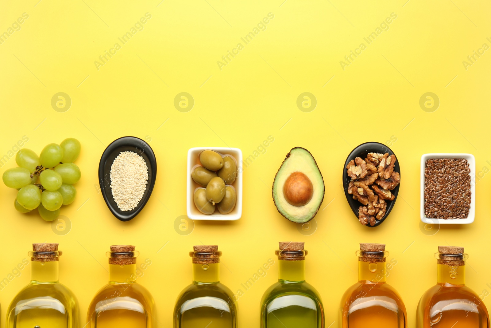 Photo of Vegetable fats. Different oils in glass bottles and ingredients on yellow table, flat lay. Space for text