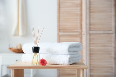 Photo of Reed air freshener and stack of towels on table against blurred background