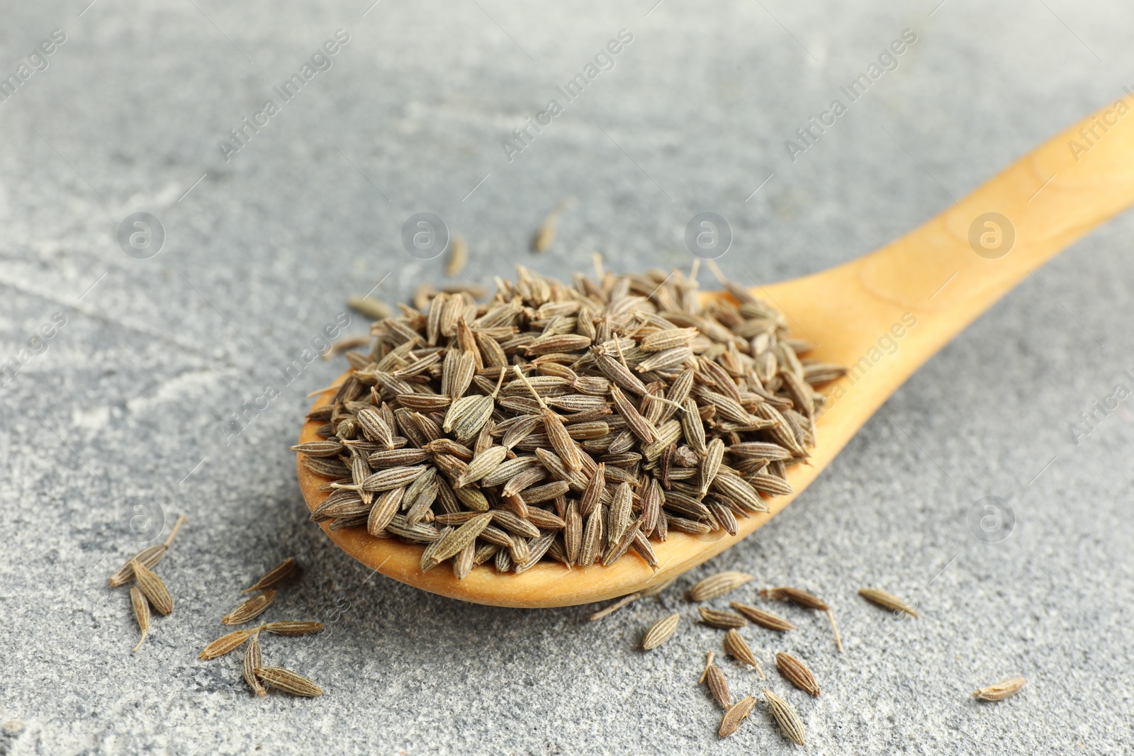 Photo of Spoon with caraway seeds on grey table, closeup