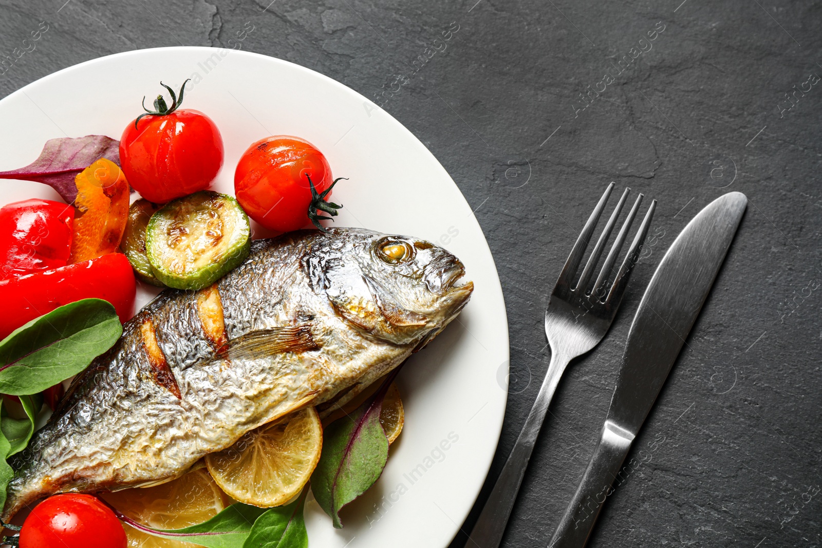 Photo of Delicious roasted fish with lemon and vegetables on dark grey table, flat lay