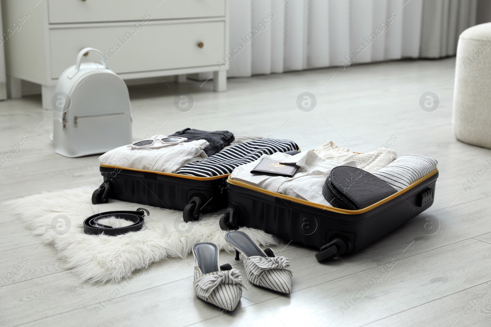 Photo of Open suitcase with clothes, shoes and accessories on floor indoors