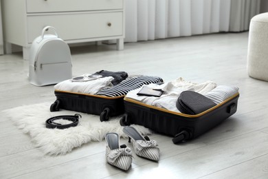 Open suitcase with clothes, shoes and accessories on floor indoors