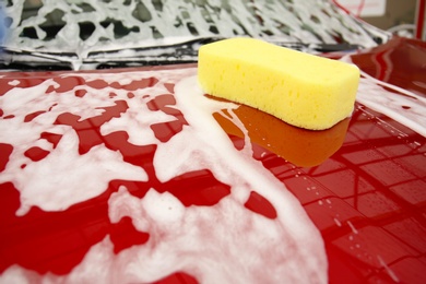 Red vehicle with foam and sponge at car wash
