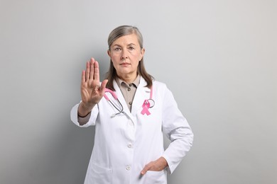 Mammologist with pink ribbon showing stop gesture on gray background. Breast cancer awareness