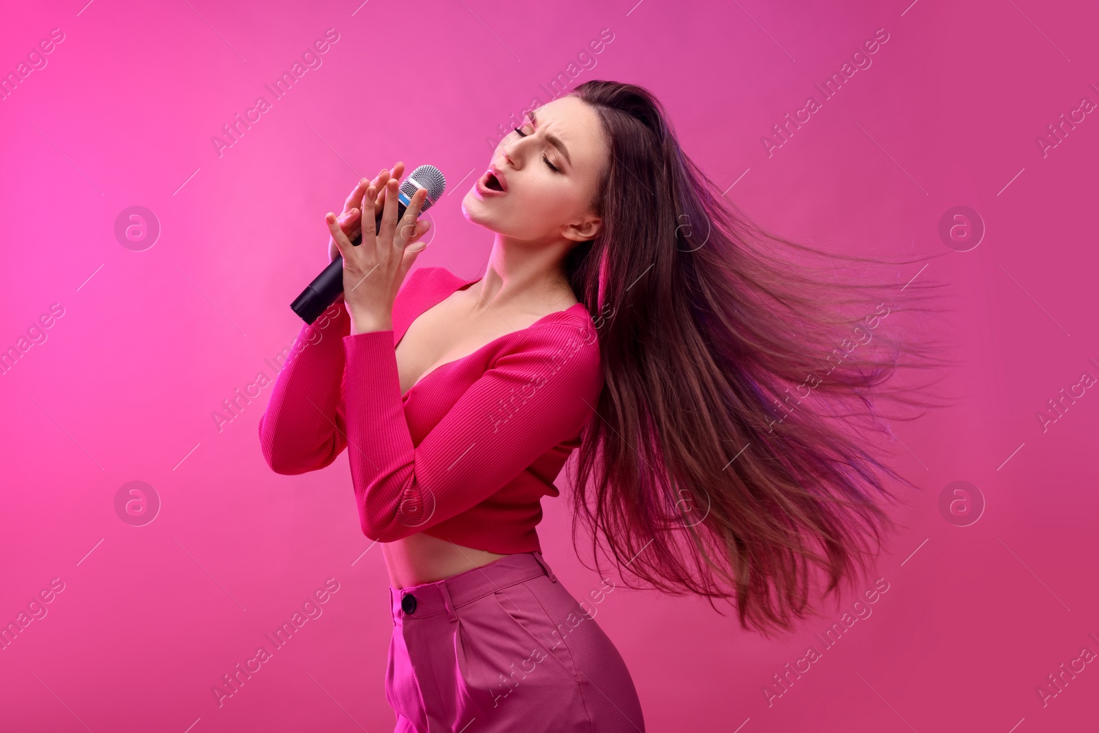 Photo of Emotional woman with microphone singing on pink background