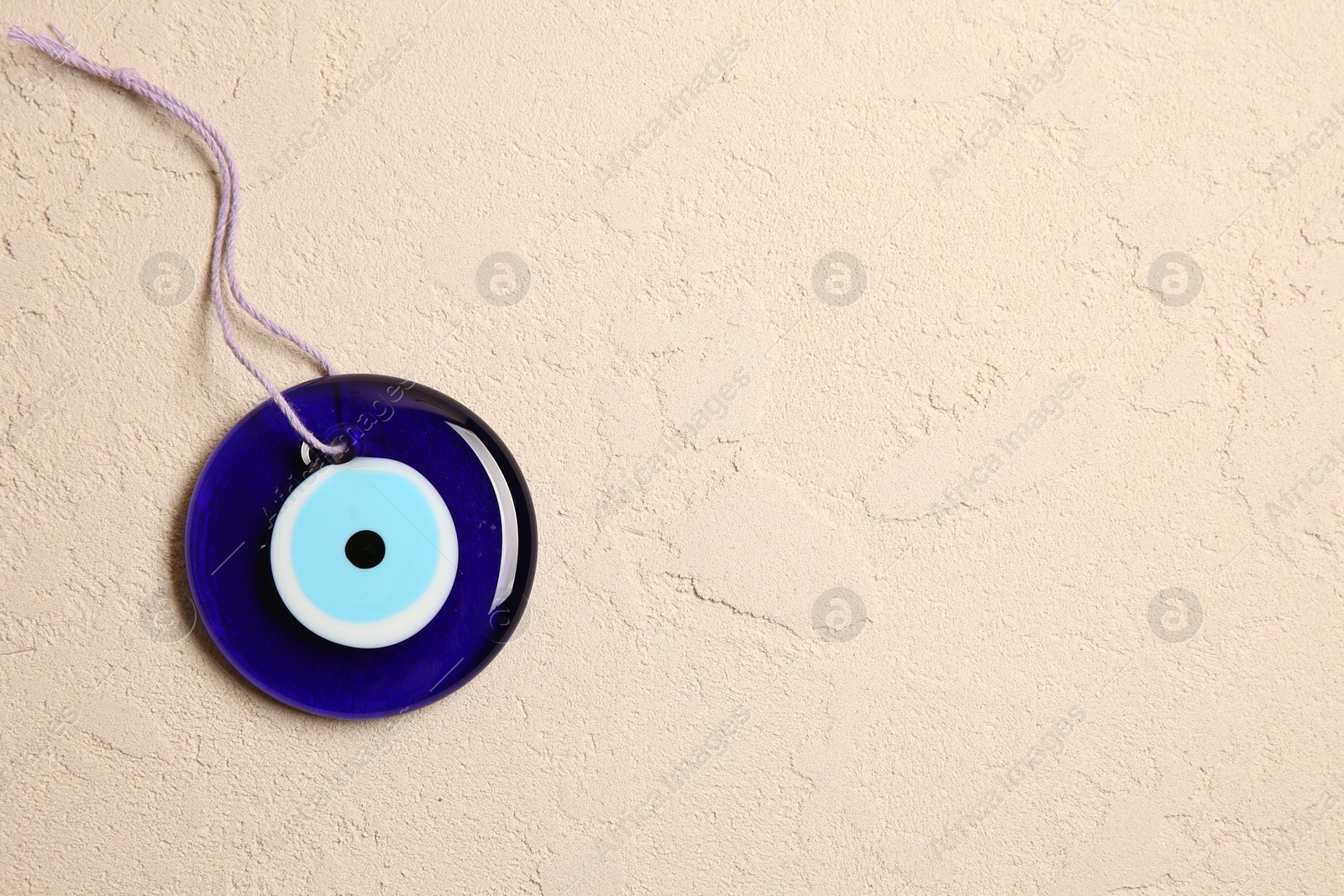 Photo of Evil eye amulet on beige textured table, top view. Space for text