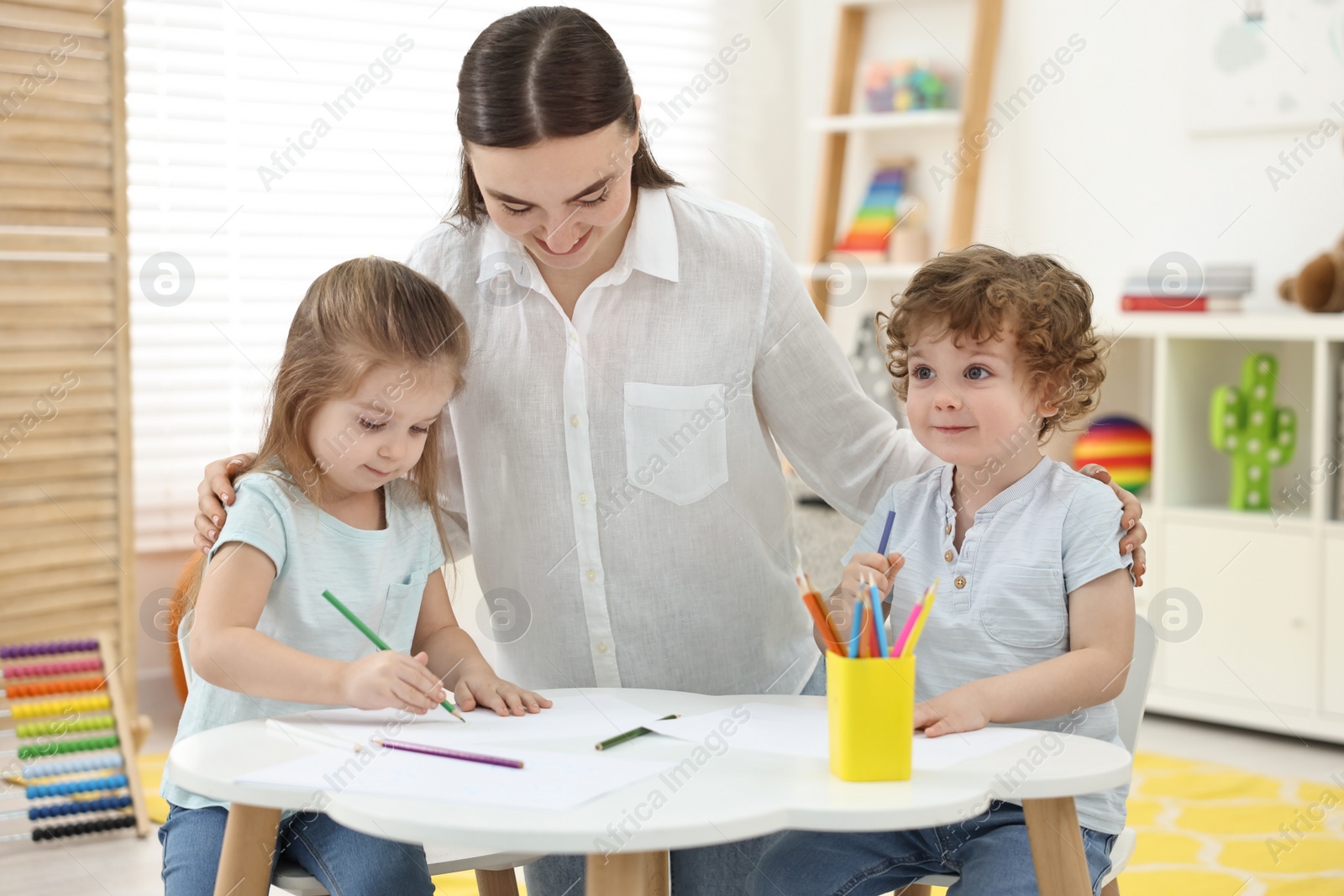 Photo of Mother and her little children drawing with colorful pencils at home