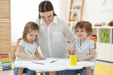Mother and her little children drawing with colorful pencils at home