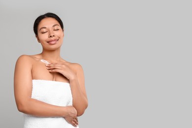 Young woman applying cream onto body on grey background. Space for text