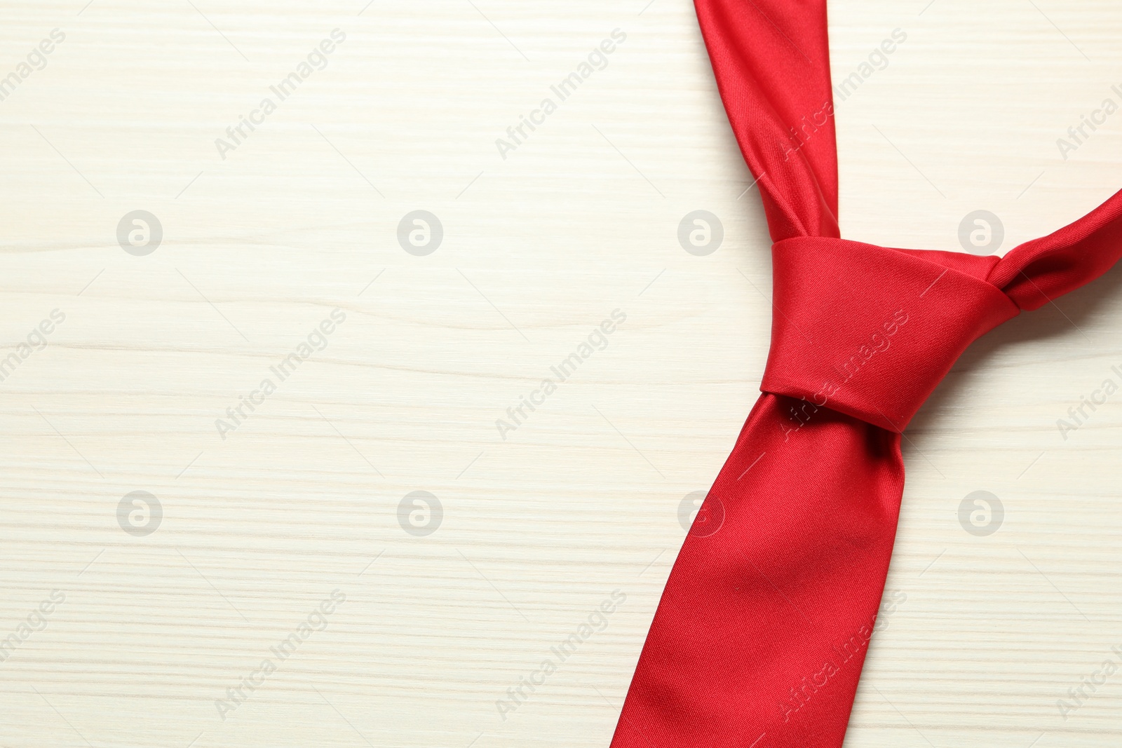 Photo of One red necktie on white wooden table, top view. Space for text