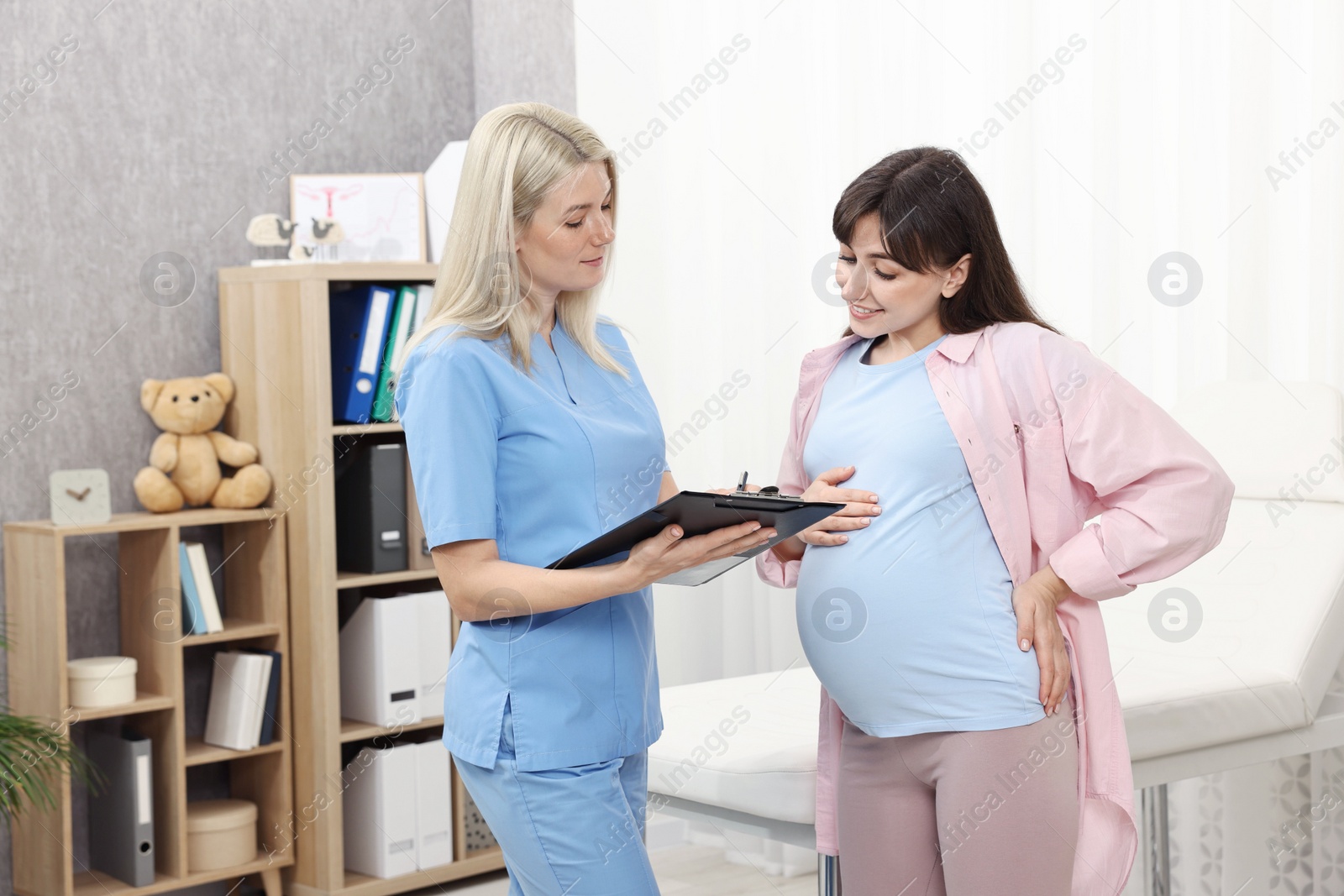 Photo of Doctor with clipboard consulting pregnant patient in clinic