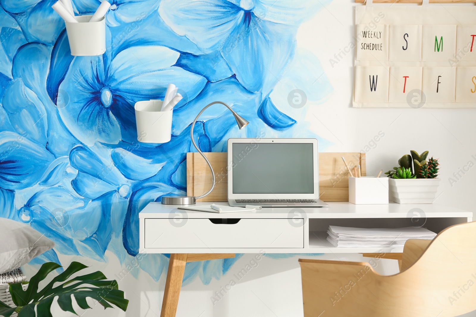 Photo of Stylish workplace with blue flowers painted on wall. Floral pattern in living room interior