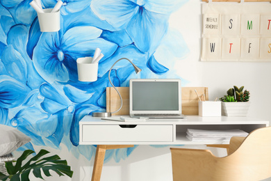 Photo of Stylish workplace with blue flowers painted on wall. Floral pattern in living room interior