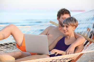 Young couple resting with laptop in hammock on beach