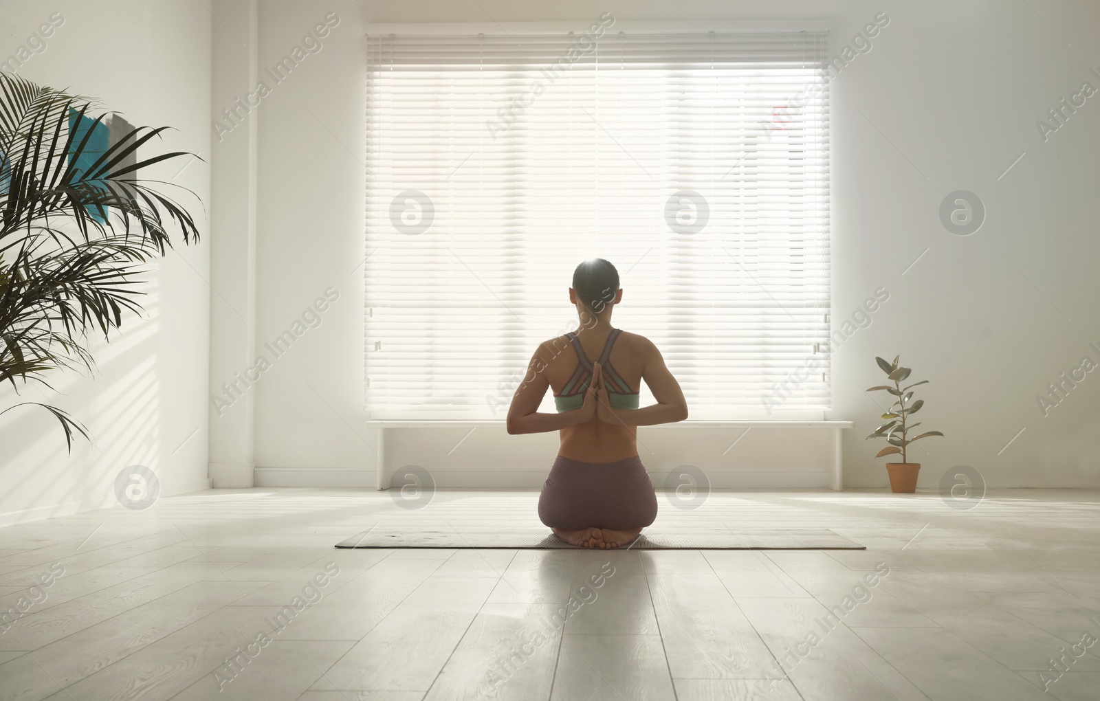 Photo of Woman practicing vajrasana with namaste behind back in yoga studio