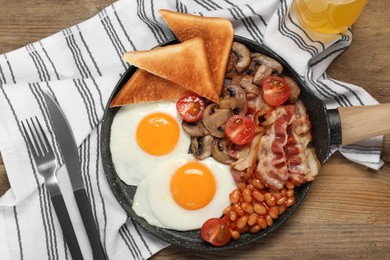 Photo of Serving pan with fried eggs, mushrooms, beans, bacon, tomatoes and toasted bread on wooden table, flat lay. Traditional English breakfast