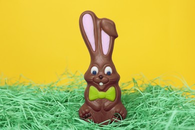 Easter celebration. Cute chocolate bunny on grass against yellow background