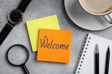 Image of Paper note with word Welcome on grey table. Office desk with stationery and coffee, flat lay