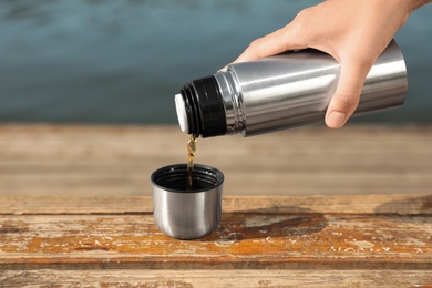 Woman pouring hot drink from thermos into cap outdoors, closeup