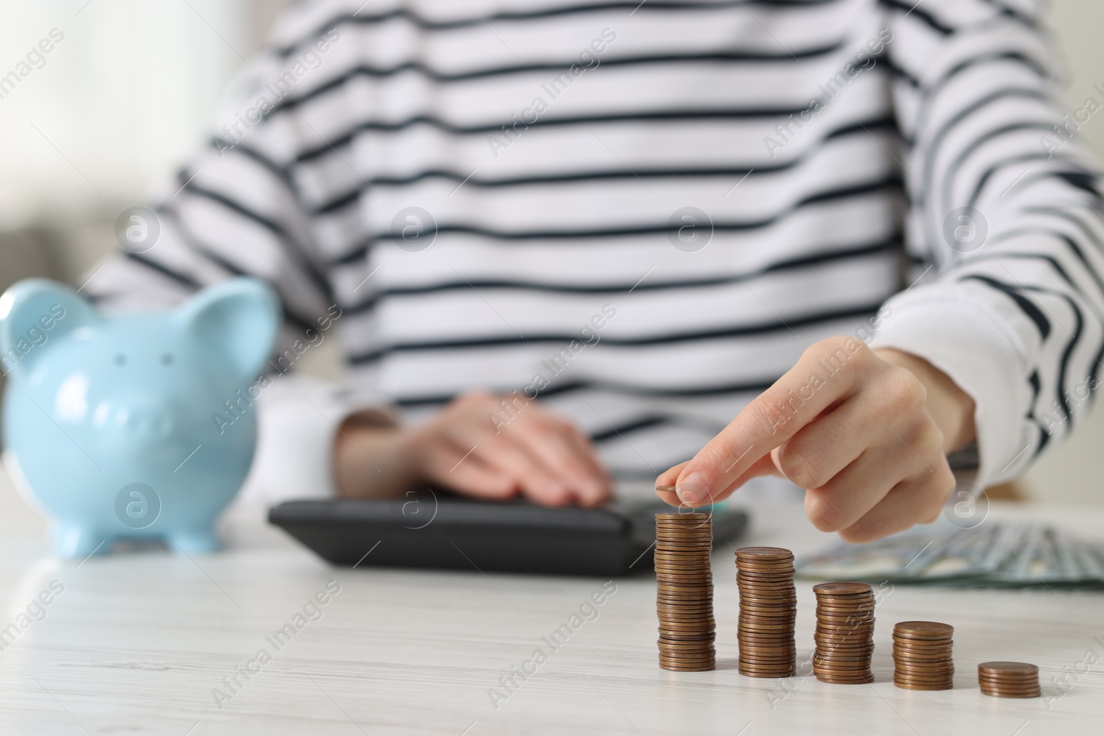 Photo of Financial savings. Woman stacking coins while using calculator at white wooden table, closeup