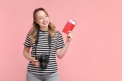 Happy young woman with passport, ticket and camera on pink background, space for text