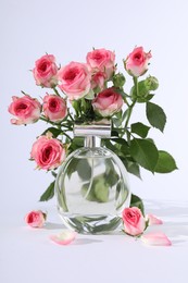 Bottle of luxury perfume and beautiful roses on white background. Floral fragrance