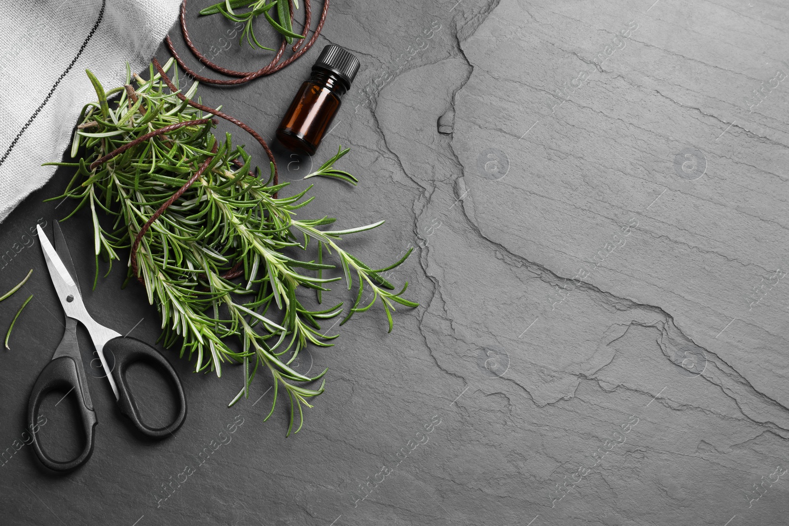 Photo of Sprigs of fresh rosemary, scissors and essential oil on black table, flat lay. Space for text