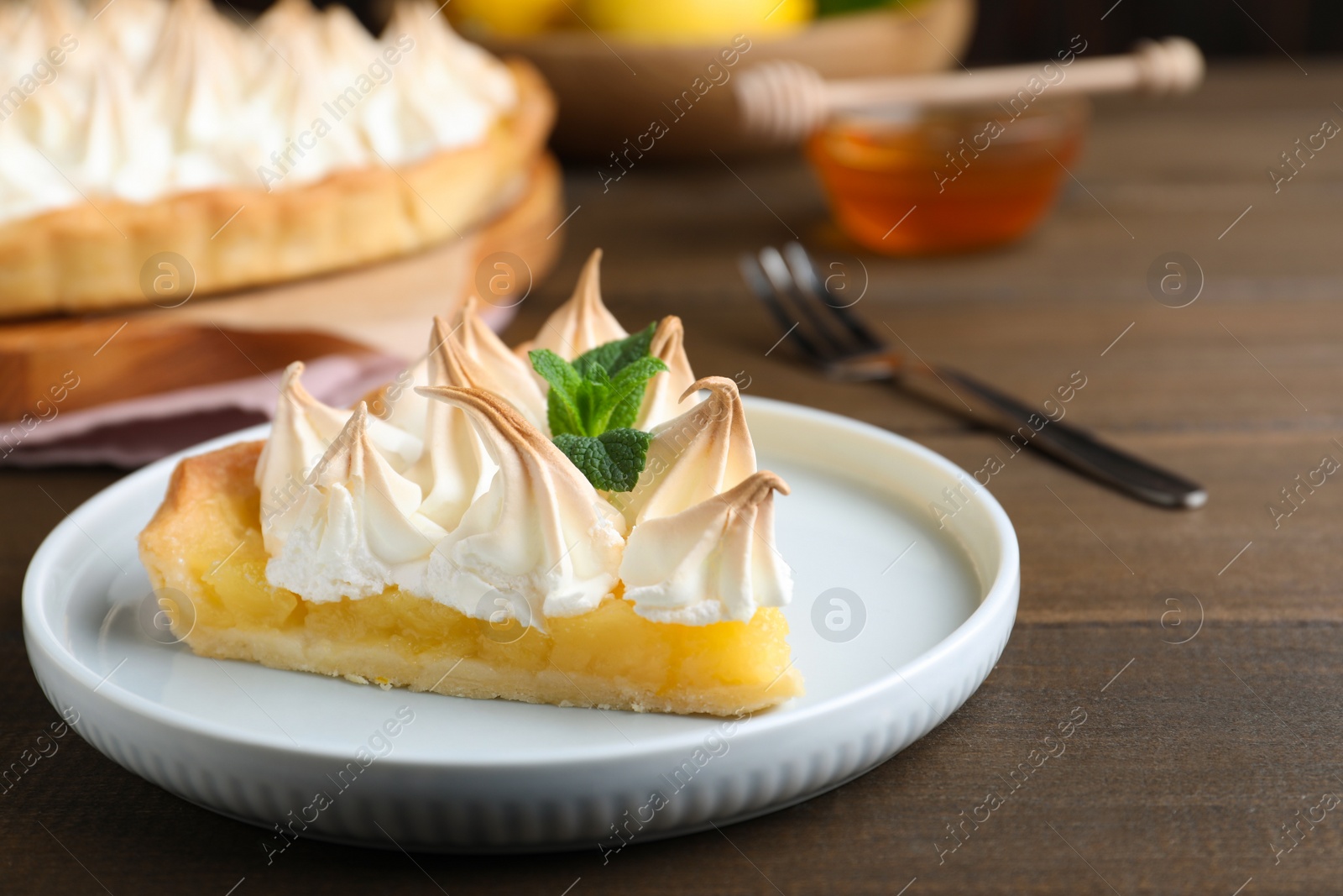 Photo of Piece of delicious lemon meringue pie with mint served on wooden table, closeup