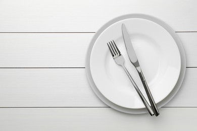 Photo of Clean plates, fork and knife on white wooden table, top view. Space for text