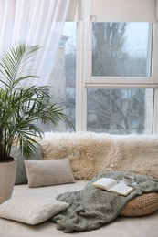 Photo of Comfortable lounge area with faux fur and pillows near window in room