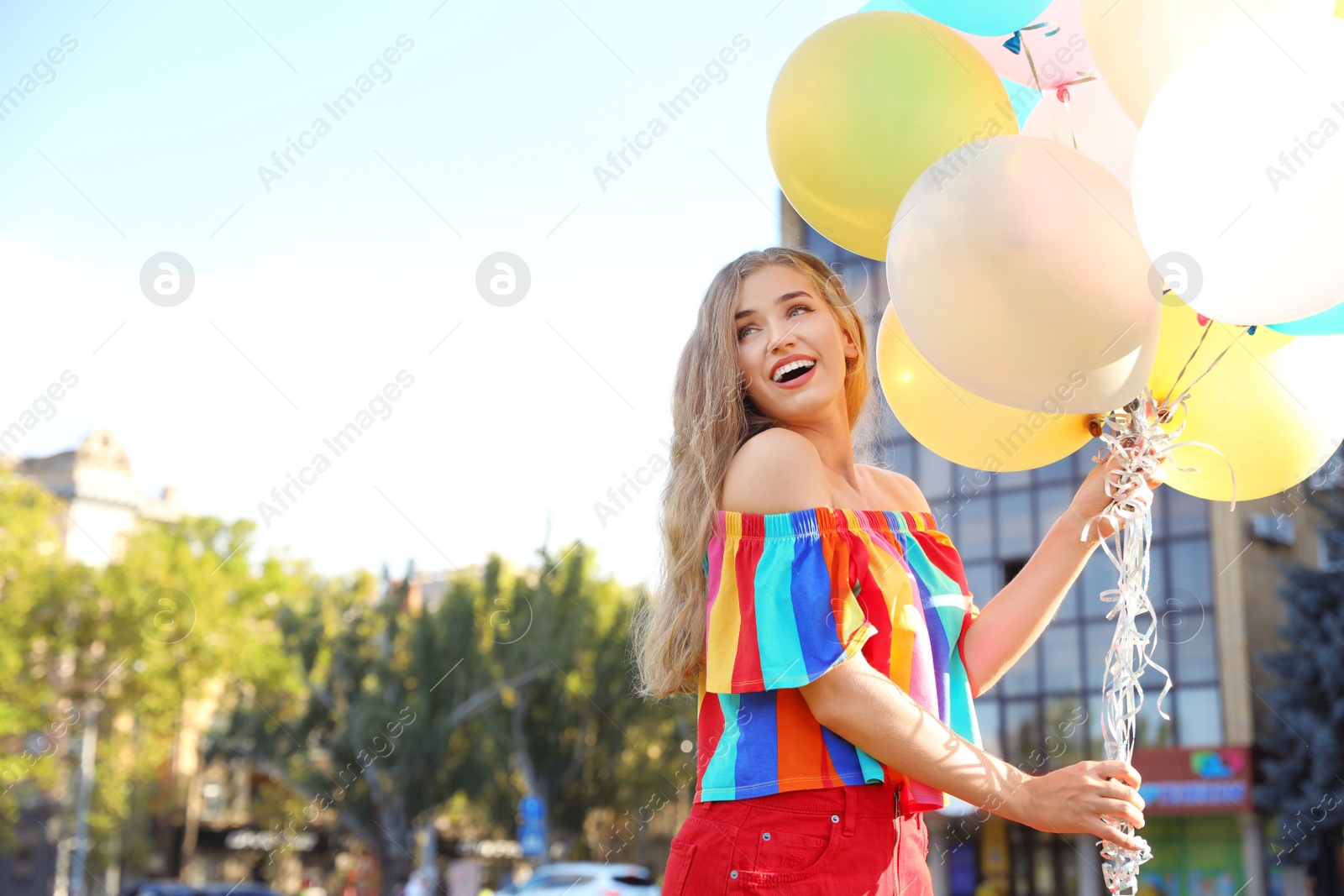 Photo of Beautiful young woman holding colorful balloons on street