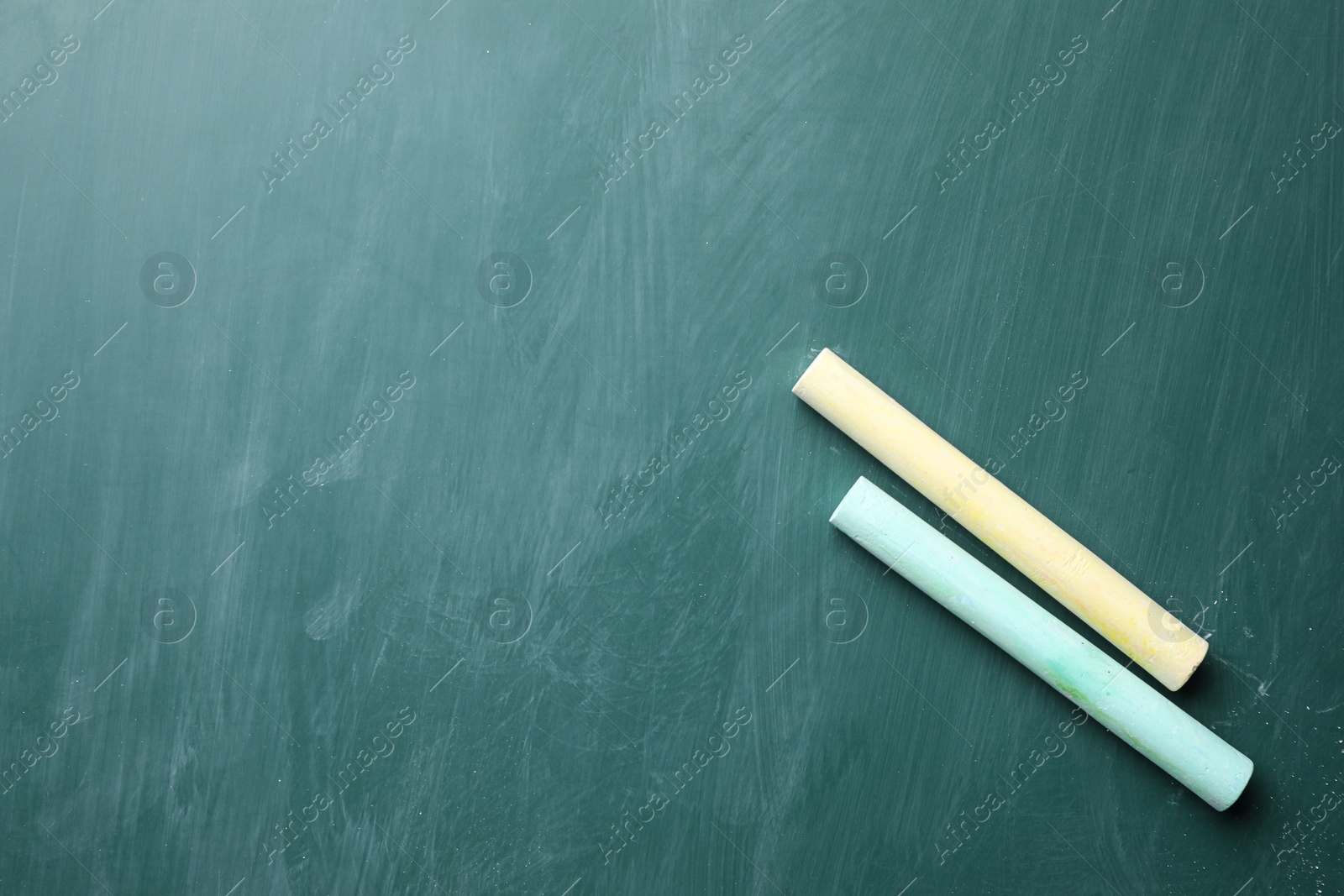 Photo of Pieces of color chalk on greenboard, flat lay. Space for text