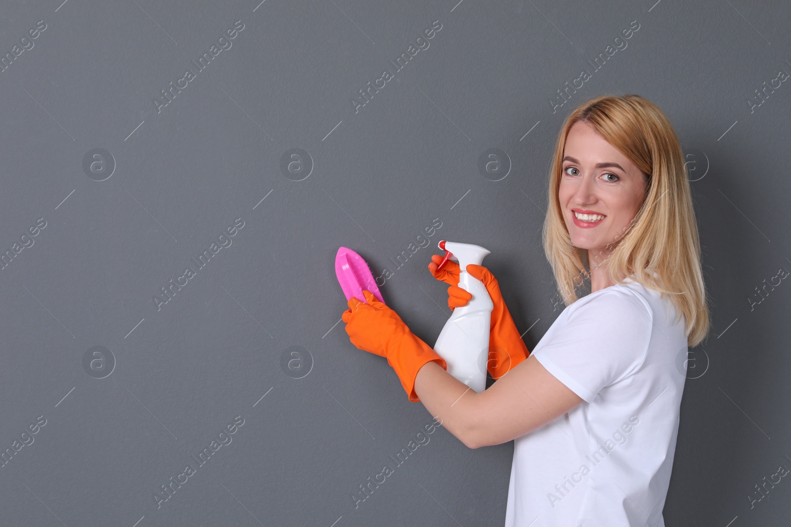 Photo of Woman in gloves cleaning grey wall with brush