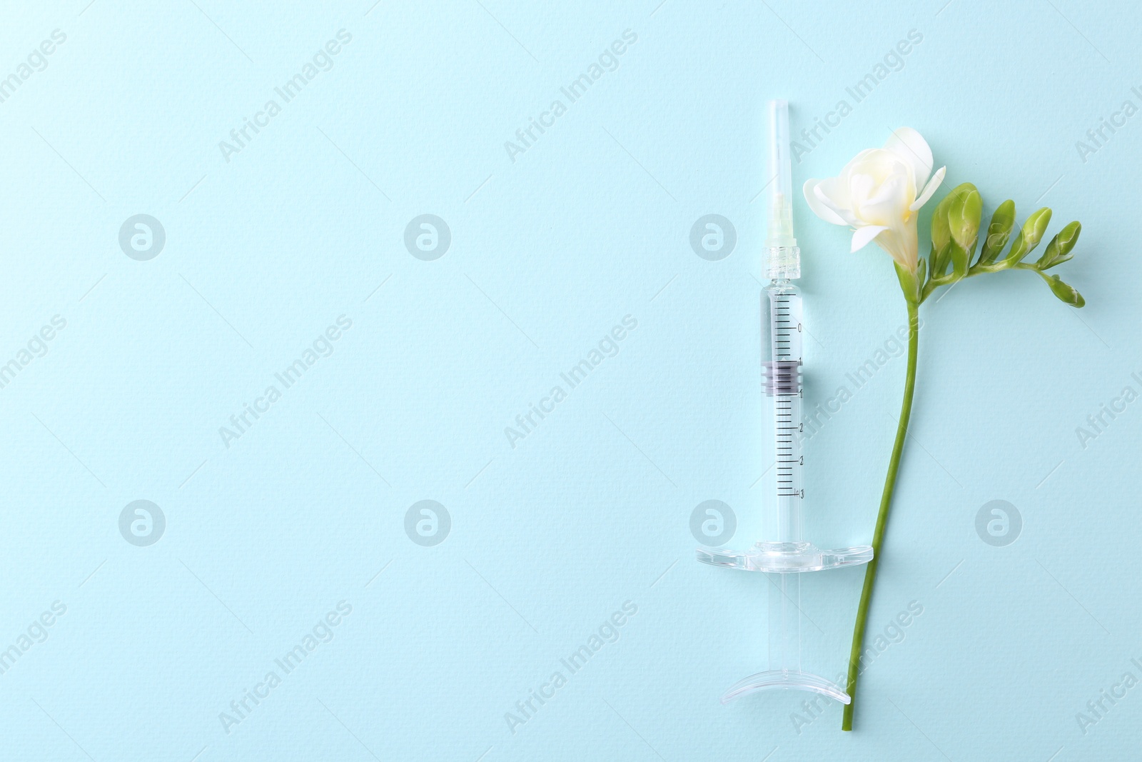 Photo of Cosmetology. Medical syringe and freesia flower on light blue background, top view. Space for text