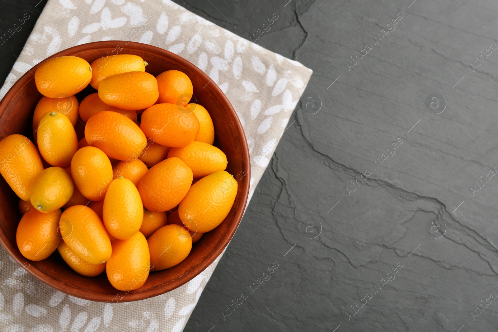 Photo of Fresh ripe kumquats in bowl on black table, top view. Space for text